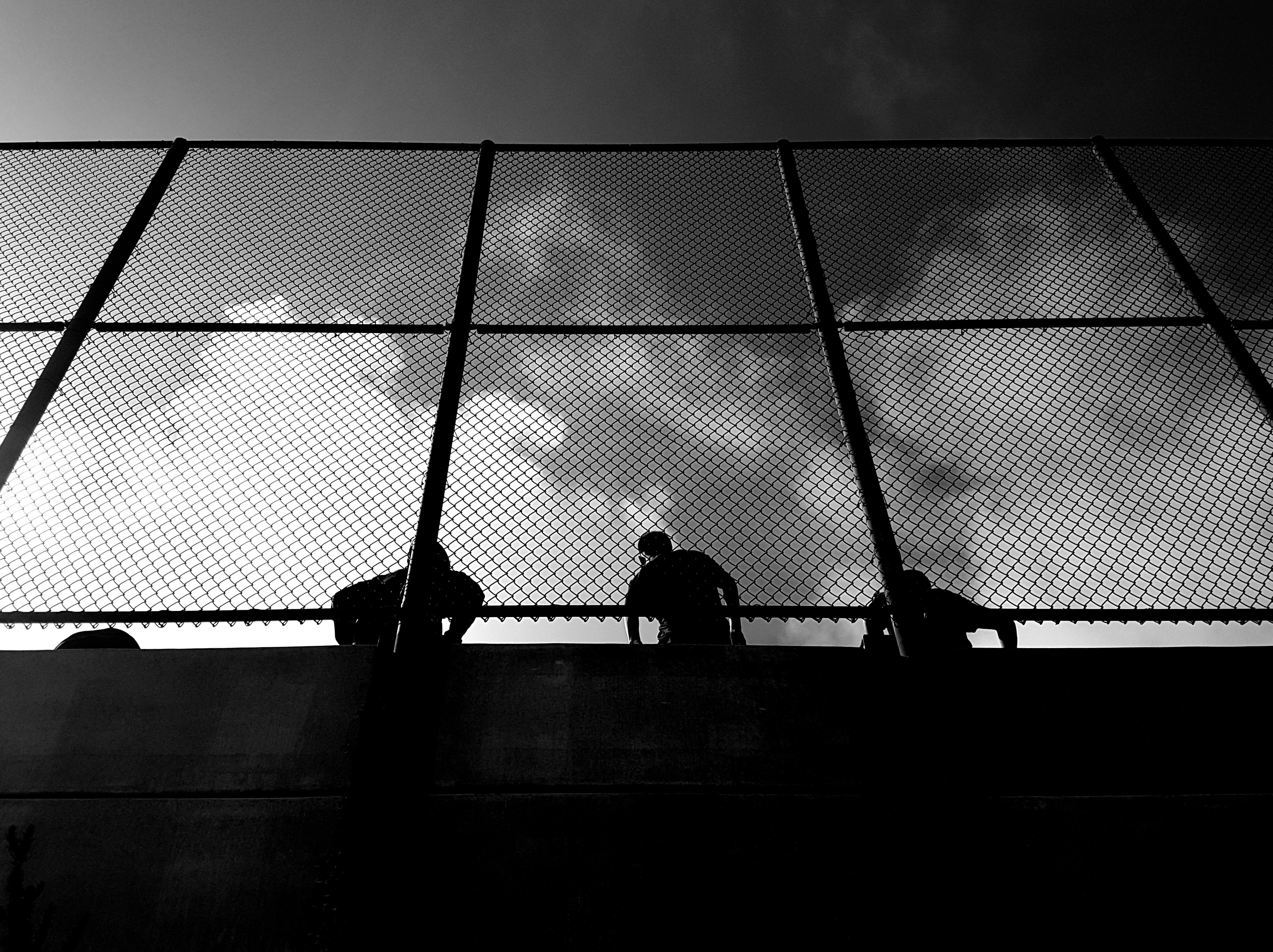 Silhouettes behind a tall fence against a cloudy sky