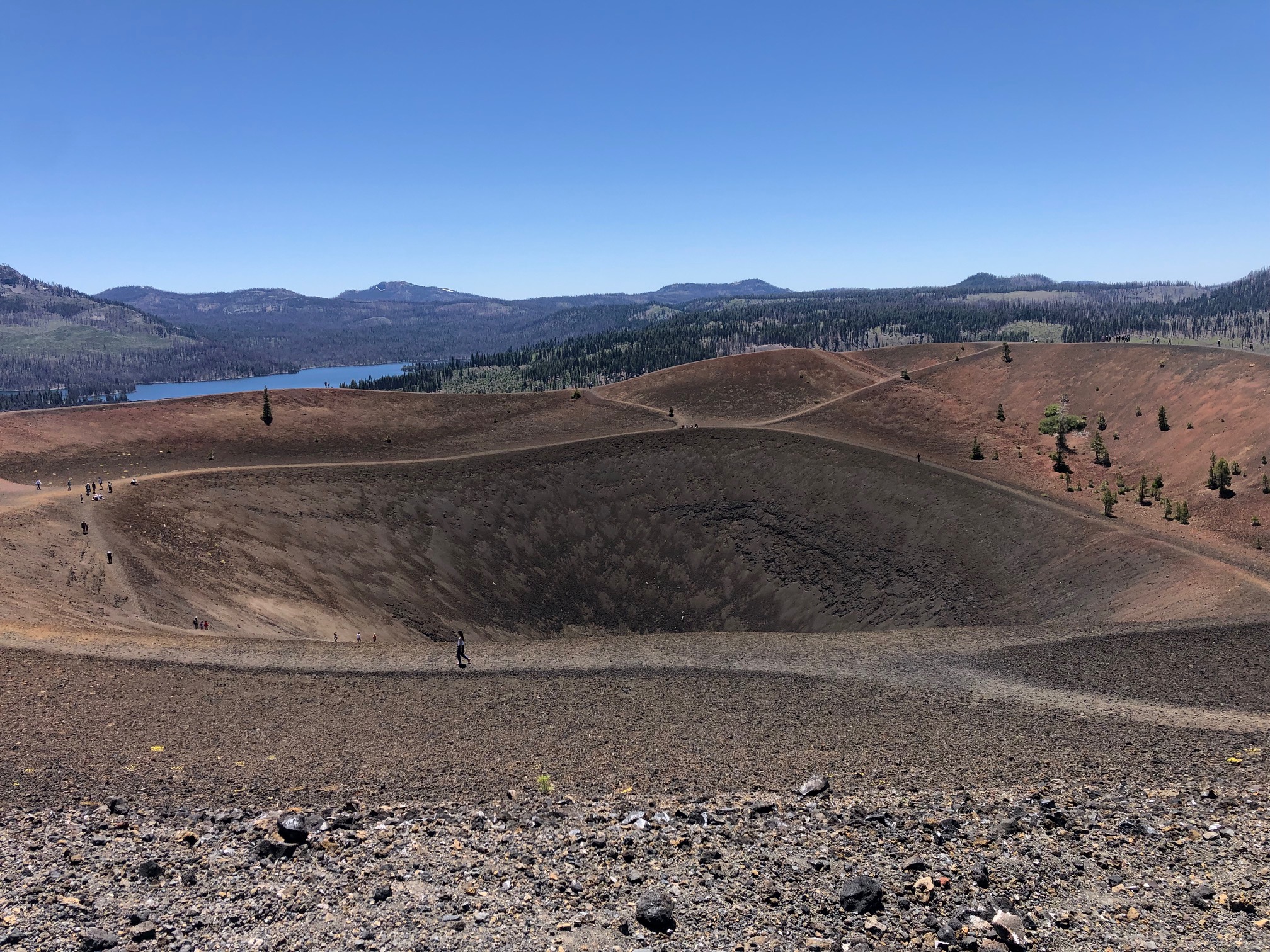 Wide volcanic crater with paths, ridges, and a distant lake